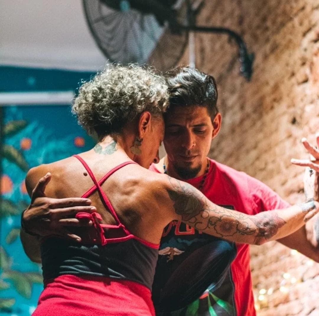 A couple in a close embrace on a milonga floor, eyes closed