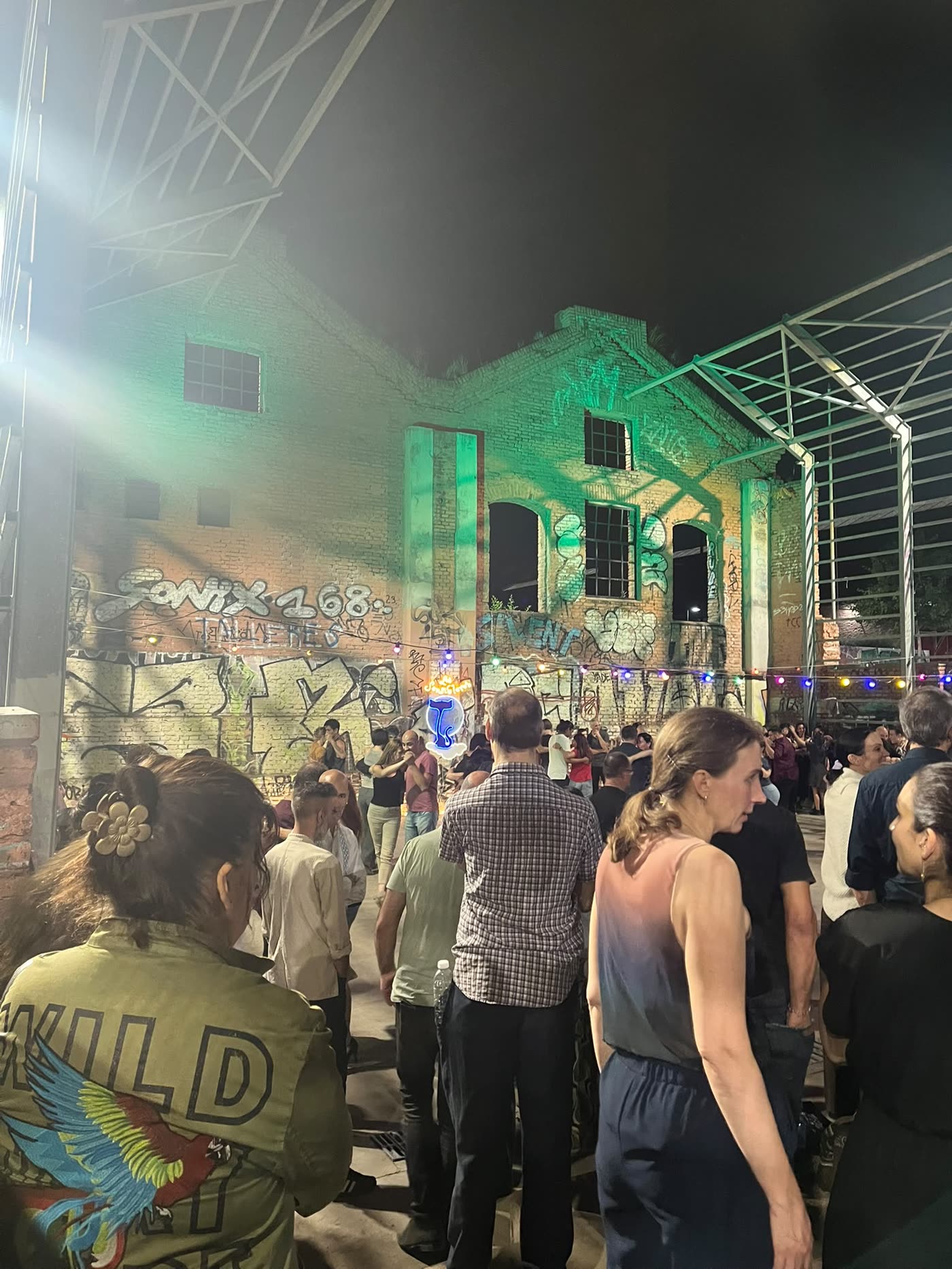People gathering in a courtyard lit green by the evening lights